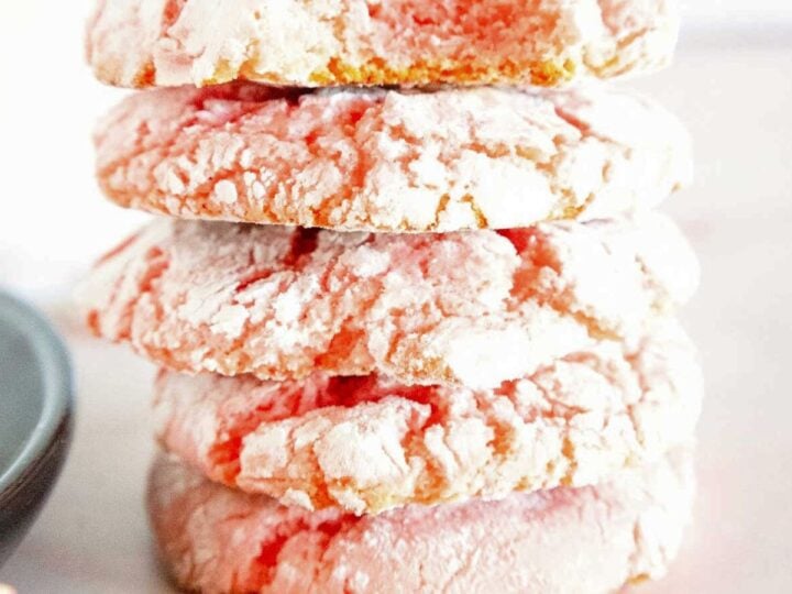 A stack of five powdered pink crinkle cookies on a white surface.