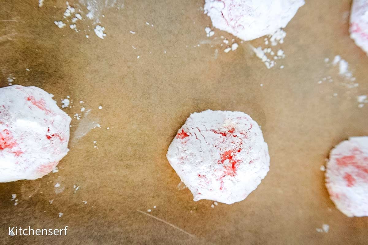 Round, red cookies coated in powdered sugar on a sheet of brown parchment paper.