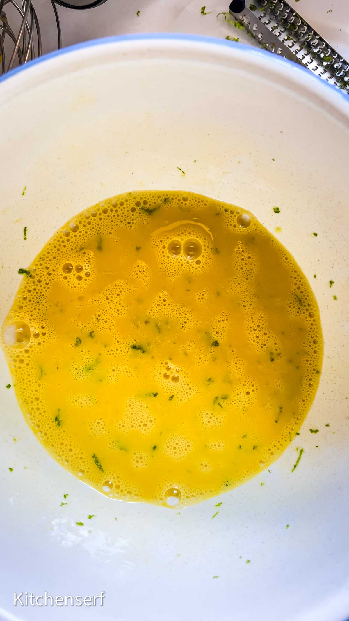 A white bowl filled with beaten eggs mixed with green zest, reminiscent of the fresh flavors found in a classic key lime pie.