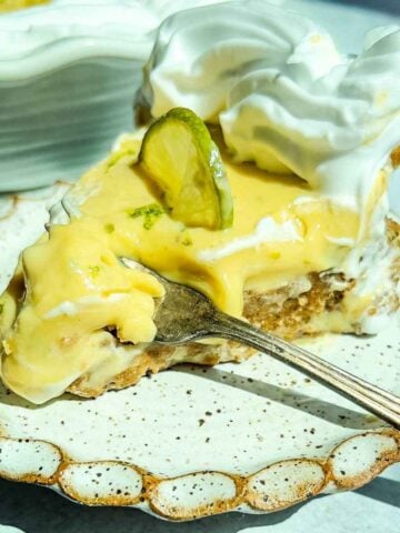 A slice of classic key lime pie with whipped cream and a lime slice, served on a ceramic plate with a fork.
