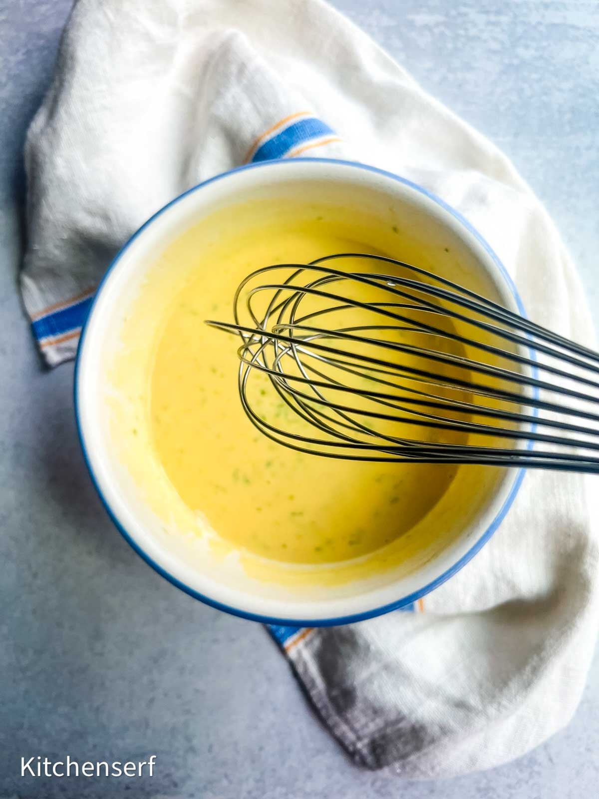 Bowl of yellow sauce, reminiscent of classic key lime pie filling, with a whisk inside, placed on a white cloth on a gray surface.