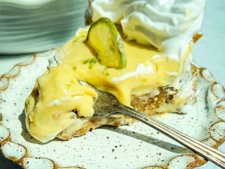 A slice of classic key lime pie with whipped cream and a lime slice, served on a ceramic plate with a fork.