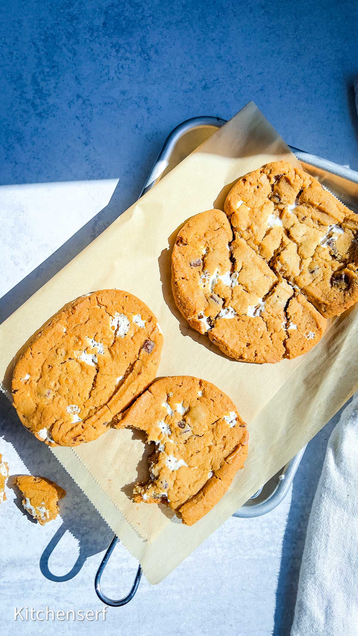Four large, golden brown S’mores cookies with marshmallow pieces rest on parchment paper, one with a bite taken out—perfect for a S’mores Cookie Dough review: buy or skip it?.