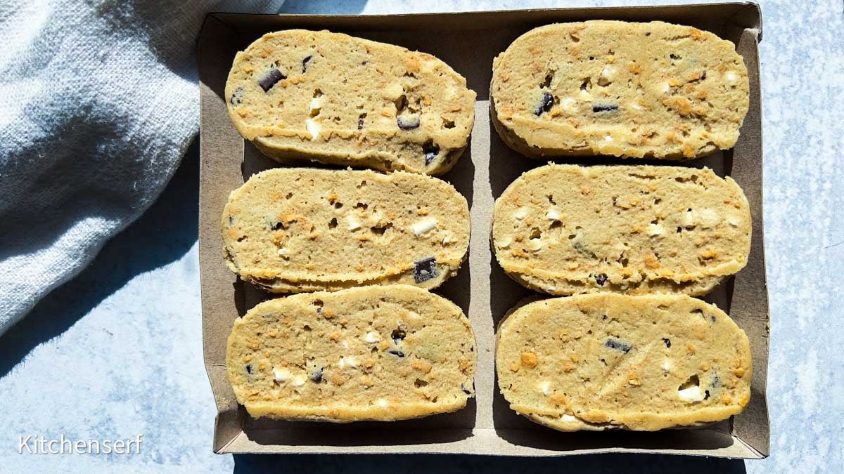 Six slices of unbaked cookie dough with chocolate chunks arranged in a cardboard tray on a light surface—perfect for a S’mores Cookie Dough review (Buy or Skip It?).