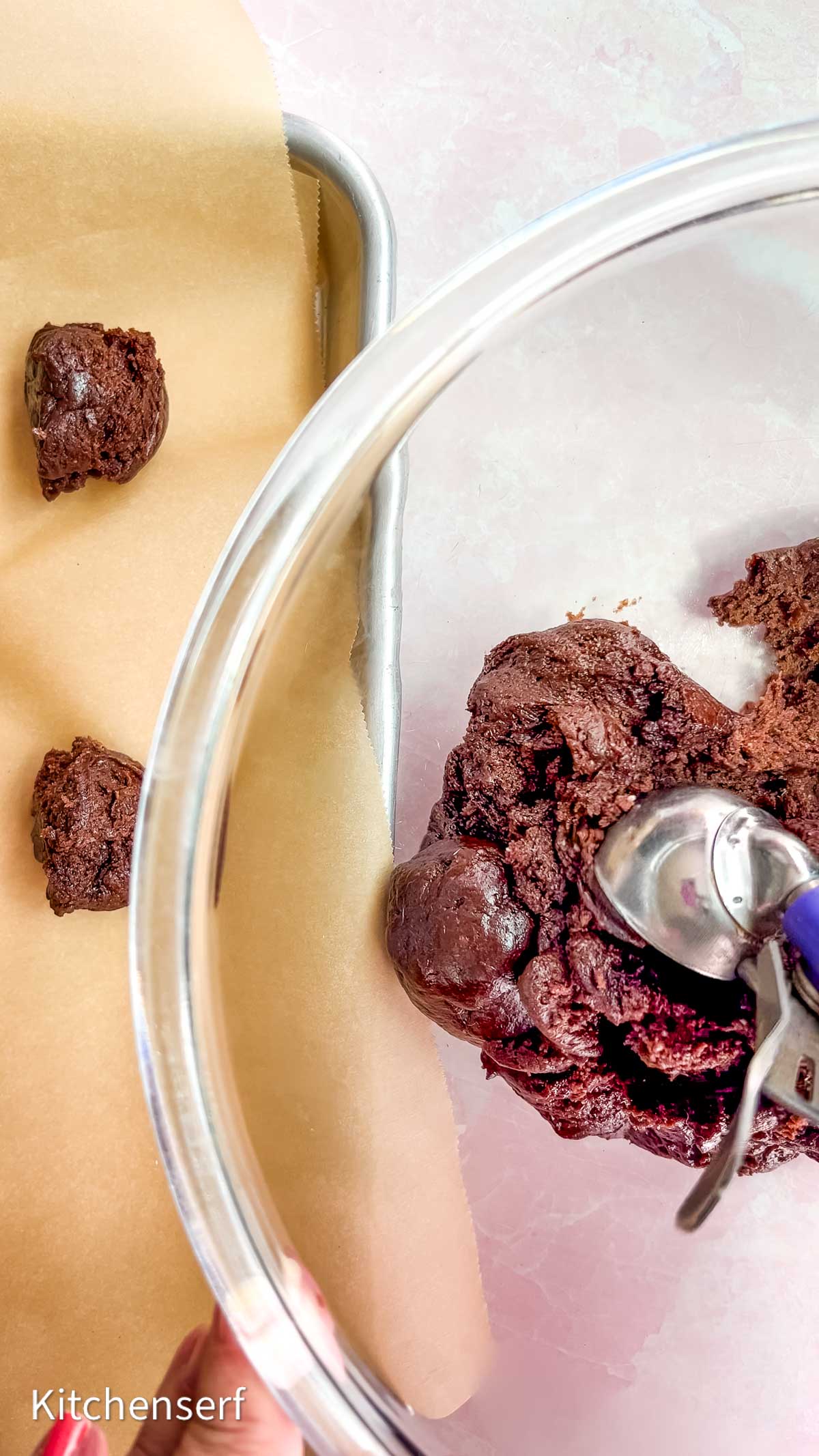 Cookie dough with a soft cake mix cookie dough texture is being scooped onto a parchment-lined baking sheet, with more dough waiting in a glass bowl.