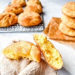 A close-up of snickerdoodle cookies, one broken in half to show the soft inside, with more cookies in the background.