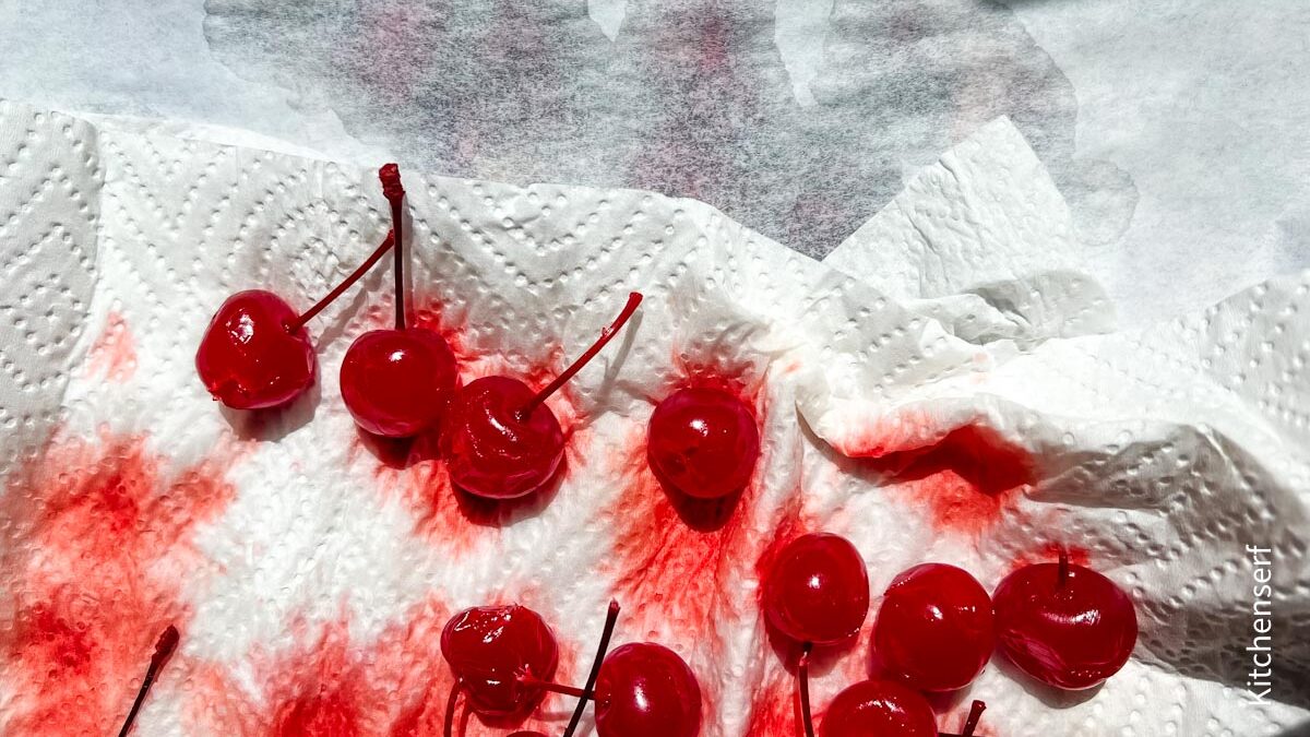 Bright red maraschino cherries with juice on white paper towels in sunlight, some cherries with stems.