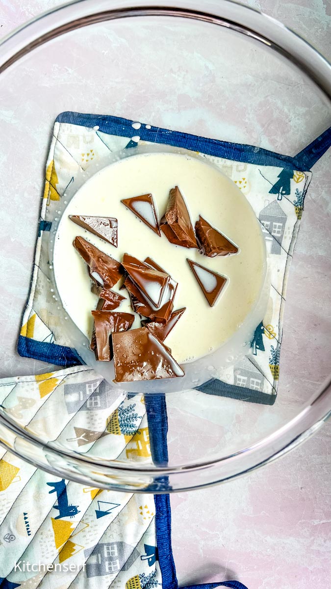A bowl with cream and broken chocolate pieces on a patterned pot holder.