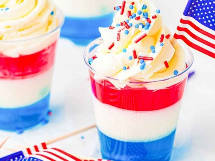 Red, white, and blue layered jello cups topped with whipped cream and festive sprinkles.
