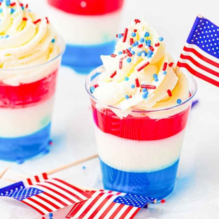 Red, white, and blue layered jello cups topped with whipped cream and festive sprinkles.