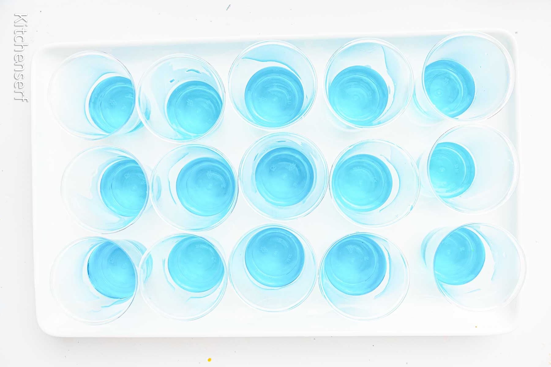A tray of small plastic cups filled with blue liquid, arranged in rows.