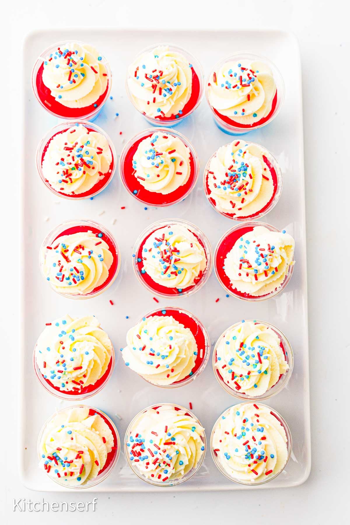 Tray of red jello shots topped with swirled whipped cream and red, white, and blue sprinkles.