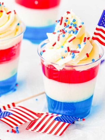 Red, white, and blue layered jello cups with whipped cream and sprinkles.