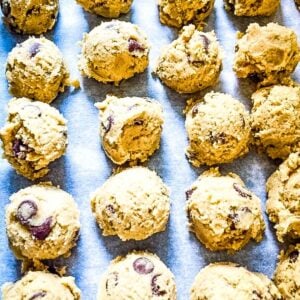 Rows of raw chocolate chip cookie dough scoops arranged on a baking sheet lined with parchment paper.