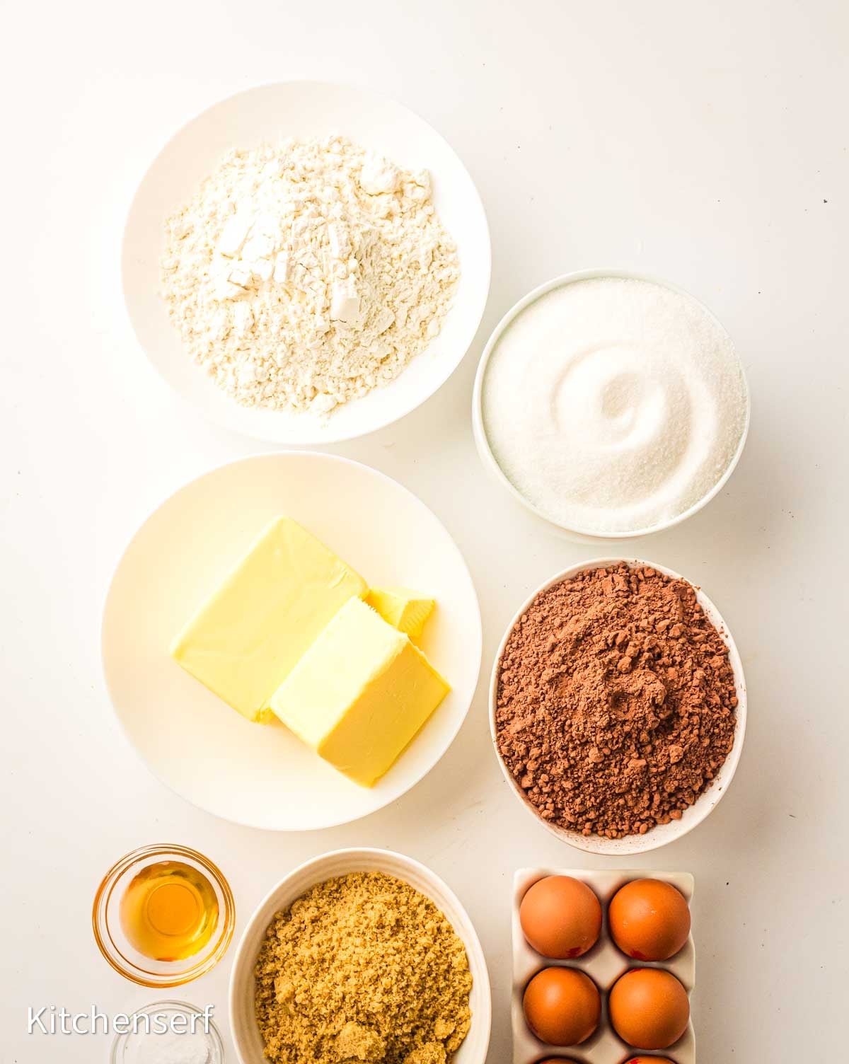 Top view of baking ingredients for brownies with cocoa powder: flour, sugar, butter, cocoa powder, brown sugar, eggs, and vanilla extract.