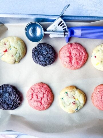 A baking sheet with assorted cake mix cookies and a blue-handled cookie scoop on parchment paper.