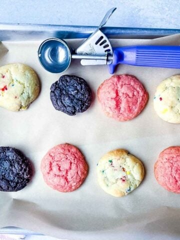 A baking tray with eight colorful half batch cake mix cookies and a purple cookie scoop on parchment paper.