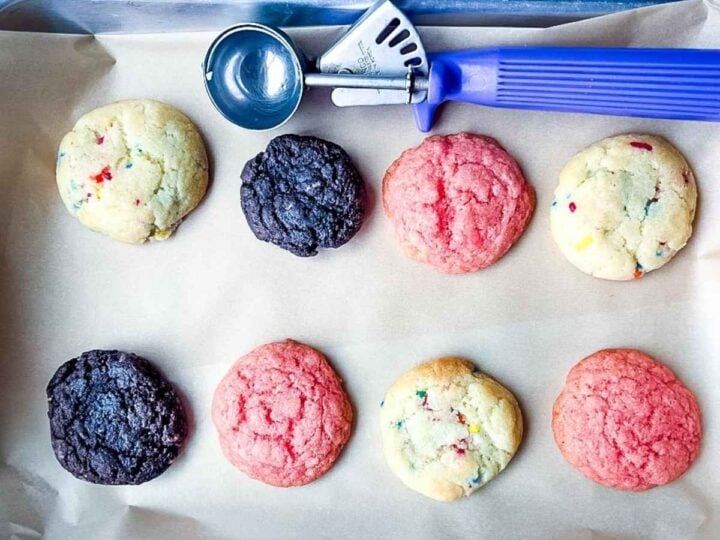 A baking tray with eight colorful half batch cake mix cookies and a purple cookie scoop on parchment paper.