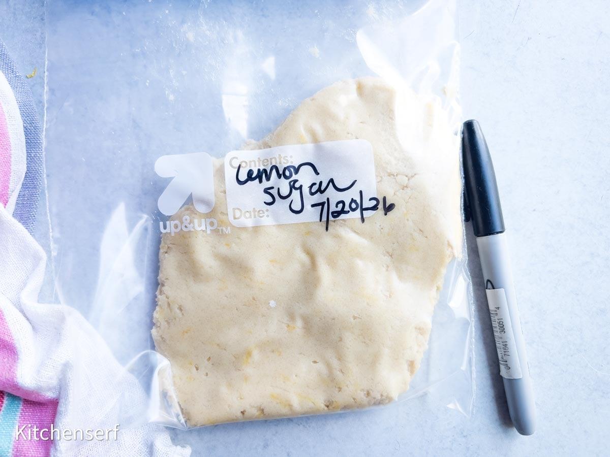 A plastic bag labeled lemon sugar with dough for soft lemon sugar cookies inside, next to a black marker on a counter.