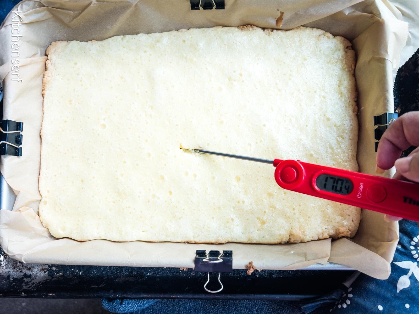 A hand checks the temperature of a freshly baked St. Louis gooey butter cake with a red digital thermometer.