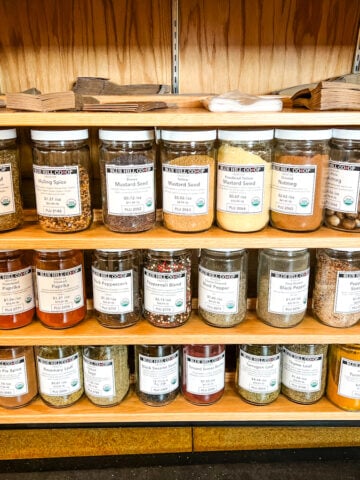 Glass jars of various spices and herbs are arranged on store shelves.