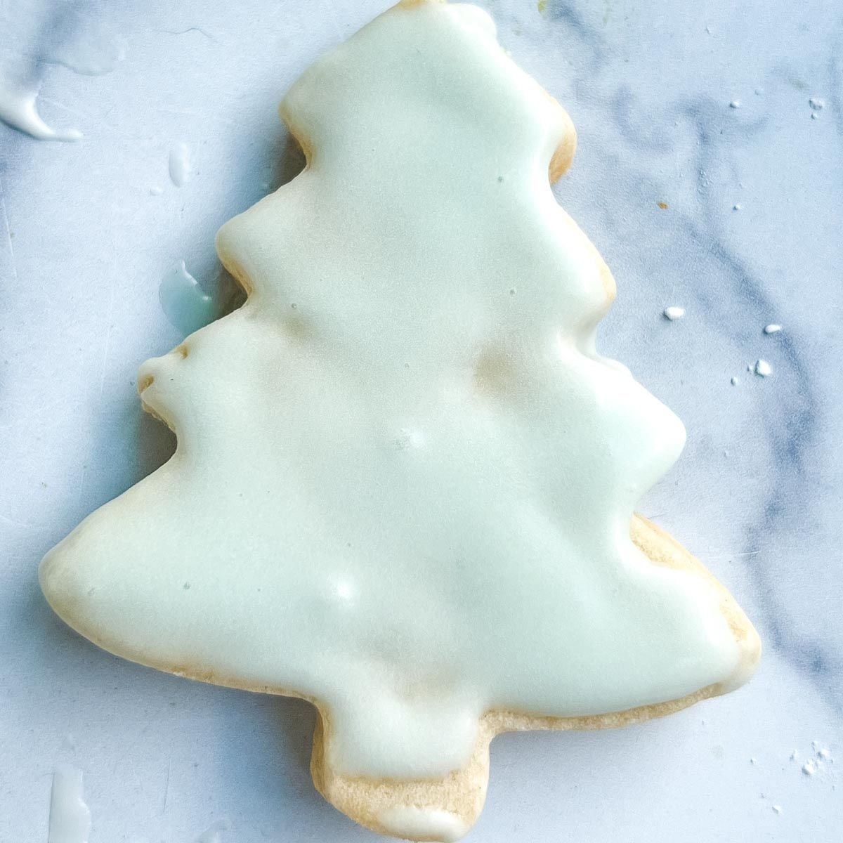 Christmas tree-shaped sugar cookie with smooth white icing on a light, marble-like background—perfect for homemade cookies for gifts.